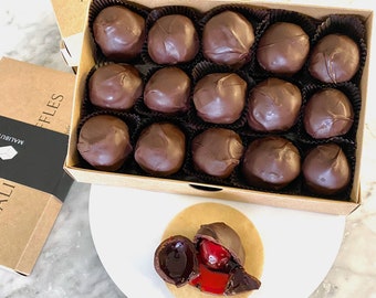 May include: A box of 16 chocolate-covered cherries. The box is brown and has the text "MALIBU" and "FFLES" on it. The cherries are arranged in a grid pattern. One cherry is shown outside the box, cut open to reveal the red cherry filling.