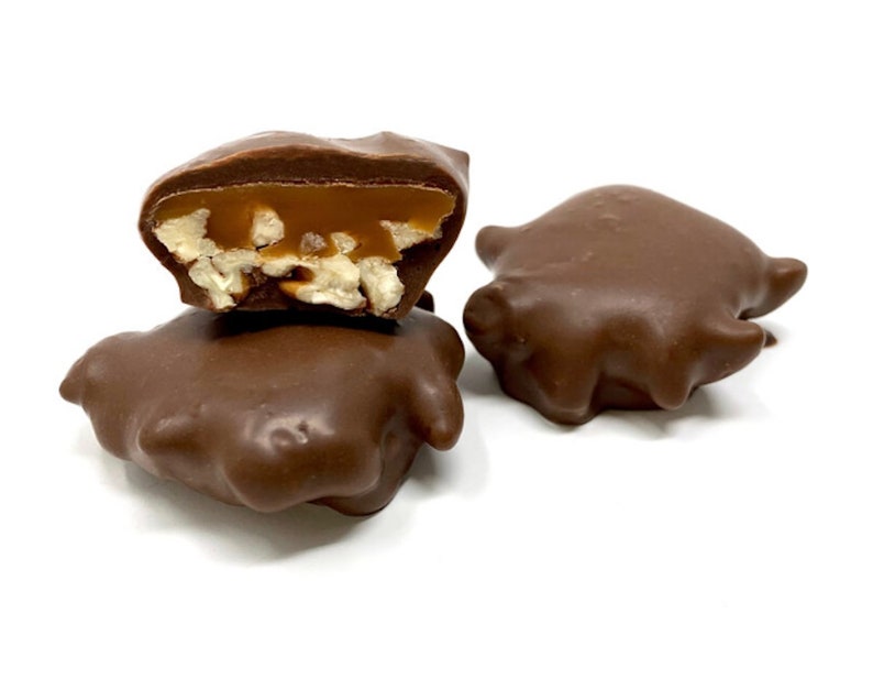 Op de afbeelding: Drie met chocolade omhulde snoepjes, waarvan er &eacute;&eacute;n doormidden is gesneden om een kern van goudkleurige karamel en lichtgekleurde stukjes noot te onthullen. De buitenkant is een gladde, stevige melkchocoladelaag met een onregelmatige vorm.