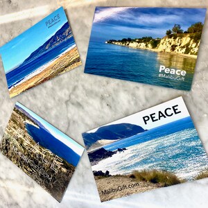Op de afbeelding: Vier rechthoekige ansichtkaarten met kustlandschappen met blauw zeewater, zandstranden en kliffen. Elke kaart toont het woord PEACE en de tekst MalibuGift.com of #MalibuGift in witte of zwarte letters over de landschappelijke beelden.