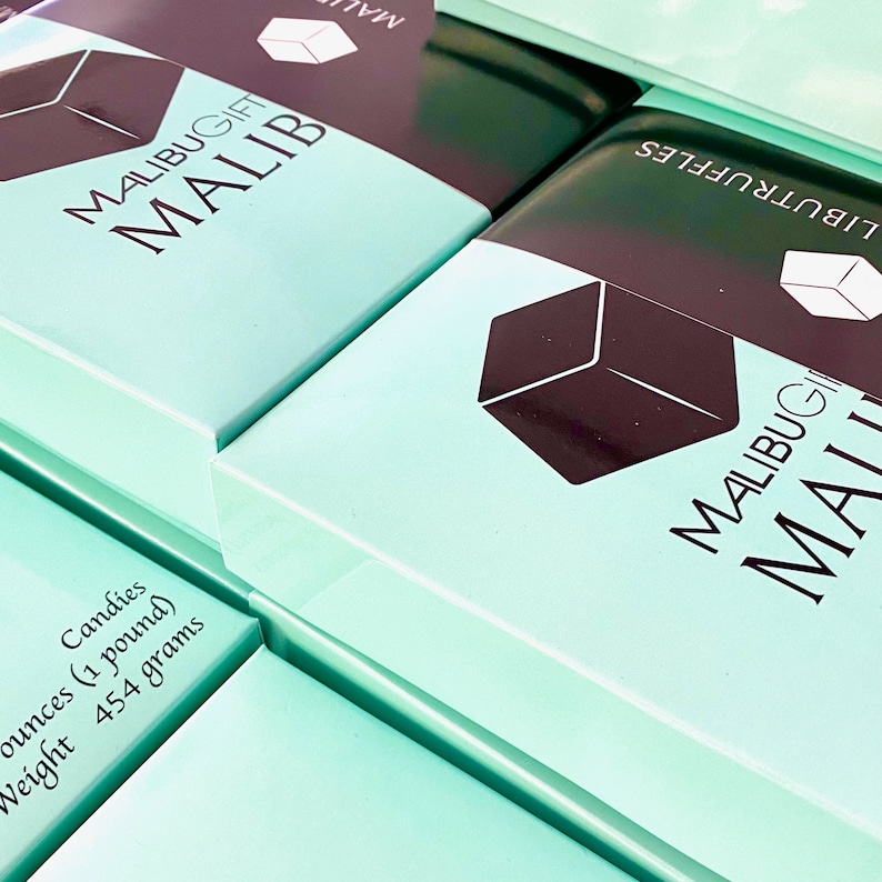May include: Stack of teal blue boxes with black lettering. The boxes are labeled "MALIBUGIFT MALIB" and "LIBUTRUFFLES". The boxes are filled with candies and weigh 1 pound or 454 grams.