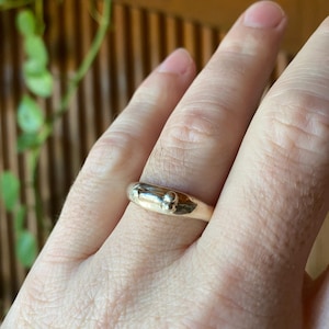 May include: A silver ring with a rounded band and a small, raised detail in the center.