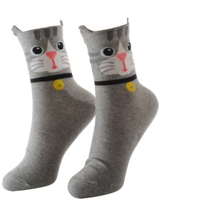 May include: A pair of gray socks with a cat face design. The cat has gray fur, pink nose, and black eyes. The socks have a black collar with a yellow button.