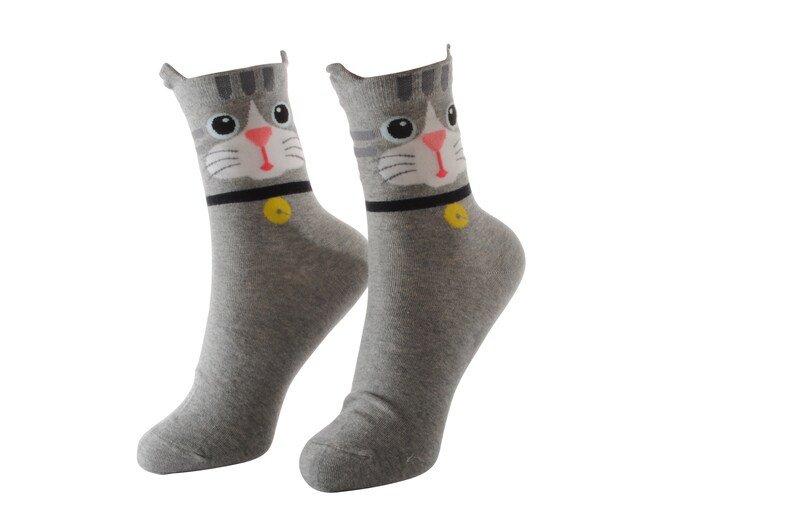 May include: A pair of gray socks with a cat face design. The cat has gray fur, pink nose, and black eyes. The socks have a black collar with a yellow button.