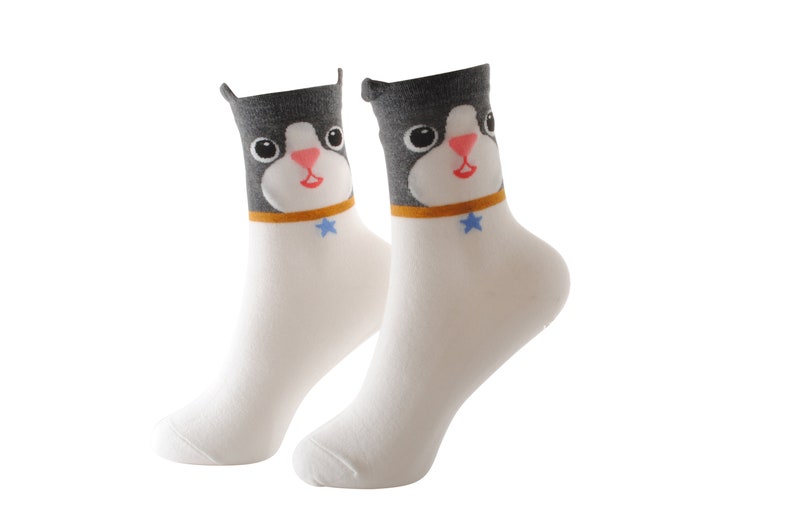 May include: A pair of white socks with a black and gray cat face design. The cat has a blue star on its collar.