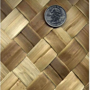 May include: Close-up of a woven, natural fiber mat with a brown and tan color scheme. A US quarter is placed on the mat for scale.