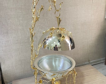 May include: A gold metal serving dish with a domed lid and a decorative stand. The stand is made of branches with gold leaves and flowers.