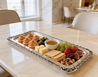 May include: A rectangular silver serving tray with an ornate scalloped edge holding an assortment of appetizers including smoked salmon on crackers, cubed cheese, green grapes, strawberries, sliced figs, nuts, and a small bowl of honey.