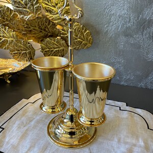 May include: Gold metal stand with two gold cups. The stand has a decorative handle and a round base.
