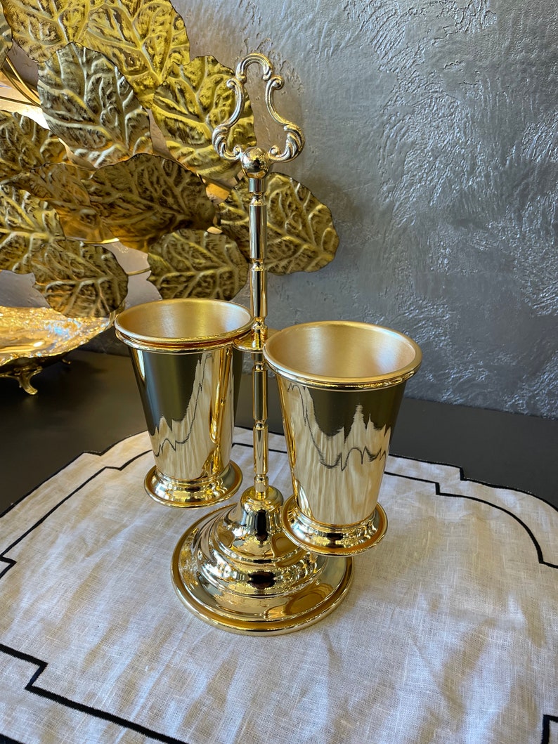 May include: Gold metal stand with two gold cups. The stand has a decorative handle and a round base.