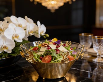 Puede incluir: Un cuenco de cristal transparente para ensalada con base de metal dorado y detalles florales dorados en el borde. El cuenco contiene una ensalada fresca con lechuga verde, tomates cherry rojos, semillas de granada, nueces y lascas de queso.