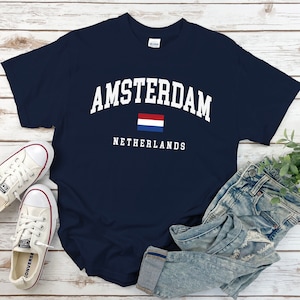 Może przedstawiać: Koszulka w kolorze granatowym z białym napisem "AMSTERDAM NIDERLANDY" i małą flagą holenderską.