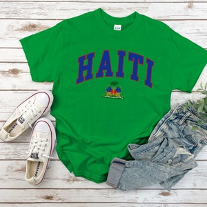 Op de afbeelding: Groen T-shirt met het woord "HAITI" in blauwe en rode letters met het embleem van de Ha&iuml;tiaanse vlag eronder.