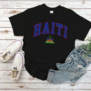 Op de afbeelding: Zwart T-shirt met een blauwe en rode "HAITI" afbeelding met de Ha&iuml;tiaanse vlag eronder.