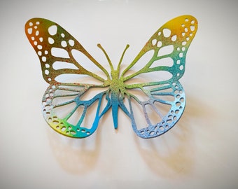 May include: A colorful butterfly cutout with a rainbow gradient and a speckled texture. The butterfly is made of paper or cardstock and has a delicate, intricate design.