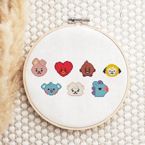 Könnte beinhalten: Ein Kreuzstich-Stickrahmen mit sieben bunten Cartoon-Charakter-Designs. Die Charaktere sind in verschiedenen Farben gehalten, darunter Rosa, Rot, Braun, Gelb, Blau und Weiß. Die Stickerei befindet sich auf einem weißen Stoffhintergrund.