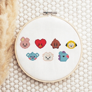 May include: A cross-stitch embroidery hoop featuring seven colorful cartoon characters. The characters are in various shapes and colors, including pink, red, brown, yellow, blue, and white. The embroidery is set in a wooden hoop.