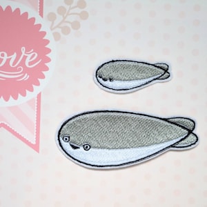 Puede incluir: Dos parches bordados con forma de ballena, uno grande y otro pequeño. Las ballenas son grises con vientres blancos y contornos negros. Los parches tienen un diseño lindo y de dibujos animados. El fondo es rosa con una pancarta rosa y blanca que dice "love".