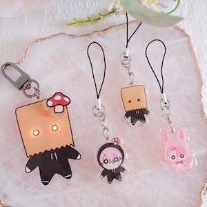 May include: A collection of acrylic charms and a keychain featuring cartoon characters. The charms include a figure with a paper bag head, a mushroom, and a pink bunny. The keychain has a silver clasp.