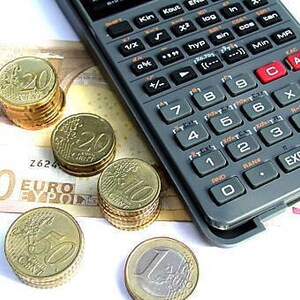 Könnte beinhalten: Ein grauer Taschenrechner mit schwarzen Tasten liegt auf einem 50-Euro-Schein und mehreren Stapeln Goldmünzen. Die Münzen haben Nennwerte von 10 und 20 Cent und einen Euro. Das Bild vermittelt ein Thema der Finanzen und des Rechnungswesens.