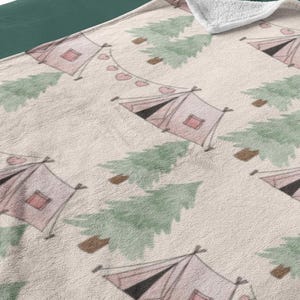 May include: A beige blanket with a repeating pattern of pink tents, green trees, and strings of pink hearts. The blanket is on a bed with green sheets and white pillows. The bed has a gray headboard.