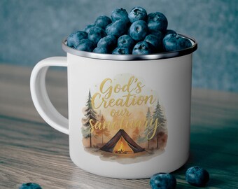 Peut inclure: Mug en émail blanc rempli de myrtilles, avec un motif doré portant l'inscription "God's Creation our Sanctuary" et une illustration à l'aquarelle d'une tente et d'arbres. Le mug a un bord argenté et une anse blanche.