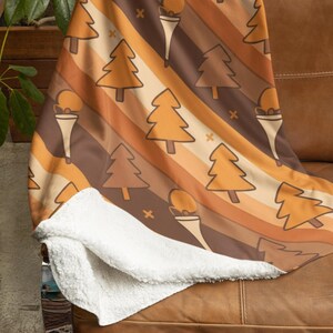 May include: A patterned throw blanket featuring a design of trees and ice cream cones in shades of brown and orange. The blanket is draped over a brown leather sofa, with a soft white sherpa lining visible.