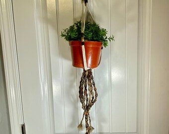 May include: A macrame plant hanger with a brown and white braided cord, holding a terracotta pot with a green plant. The hanger is attached to a white door.