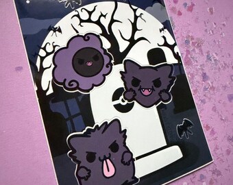 Op de afbeelding: Een sticker met een griezelige kerkhofscène met een volle maan, vleermuizen en drie paarse cartoongeesten. De sticker heeft een donkerblauwe achtergrond en de tekst "dark Dreamer".
