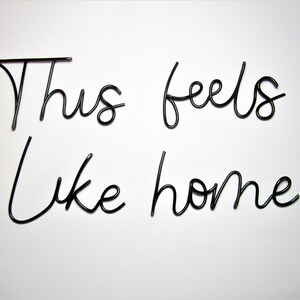 May include: Black metal wire wall decor with the words "This feels like home" in a cursive font.