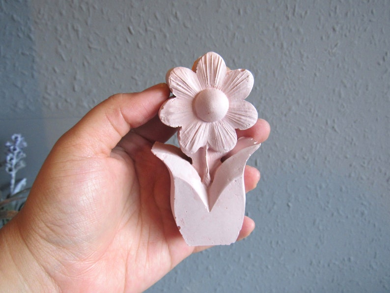 K&ouml;nnte beinhalten: Eine rosafarbene Keramik-Blumenskulptur mit einer einzelnen Bl&uuml;te und Bl&auml;ttern. Die Bl&uuml;te hat eine runde Mitte und f&uuml;nf Bl&uuml;tenbl&auml;tter.