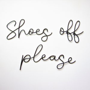 May include: Black wire sculpture sign that reads "Shoes off please".