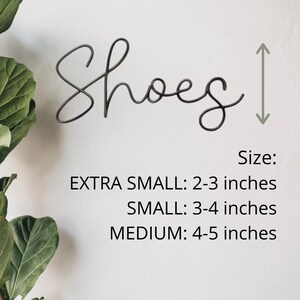 May include: Metal wall decor with the word "Shoes" in a cursive font. The sign is 2-3 inches tall when extra small, 3-4 inches tall when small, and 4-5 inches tall when medium.