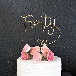 May include: Gold wire cake topper that says "Forty" with pink flowers on a white cake.