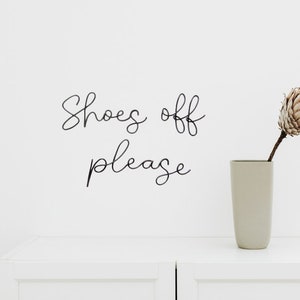 May include: White wall with black cursive lettering that reads "Shoes off please" and a beige vase with a dried flower arrangement.