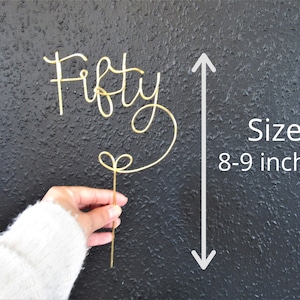 May include: Gold wire cake topper that says "Fifty" in a cursive font. The topper is 8-9 inches tall.