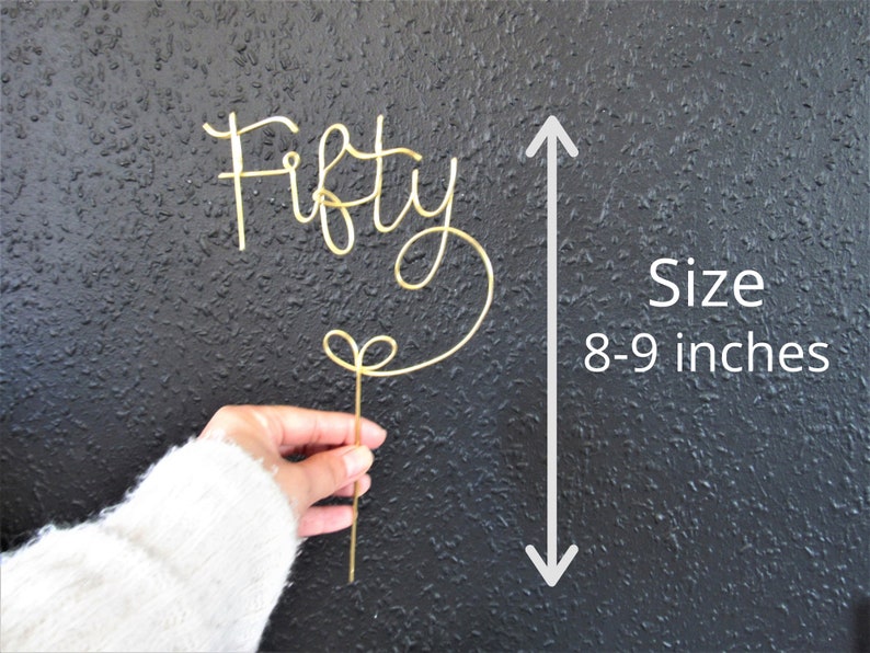 May include: Gold wire cake topper that says "Fifty" in a cursive font. The topper is 8-9 inches tall.