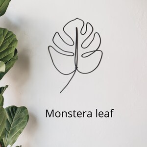 May include: A black wire sculpture of a monstera leaf on a white background. The text "Monstera leaf" is written below the sculpture.