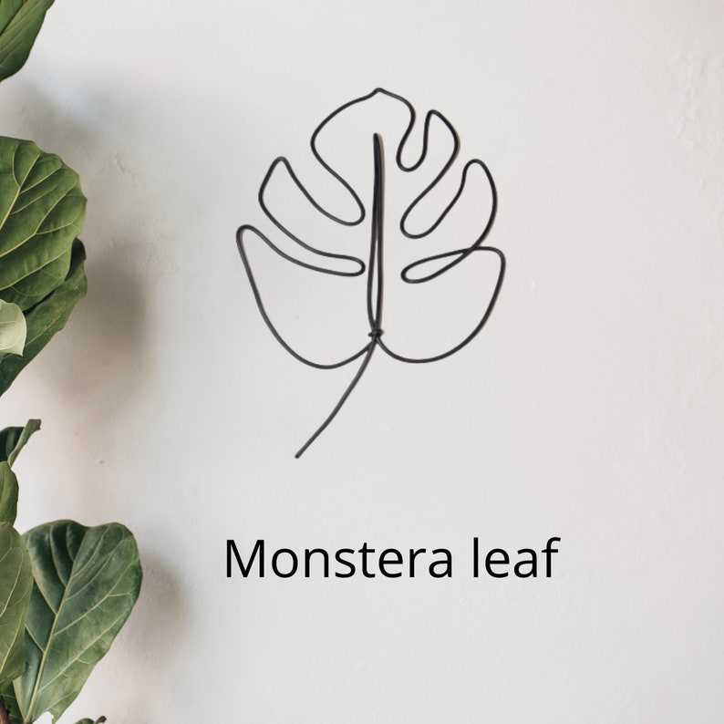 May include: A black wire sculpture of a monstera leaf on a white background. The text "Monstera leaf" is written below the sculpture.