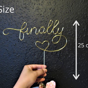 May include: Gold wire cake topper that says "finally" with a heart at the end. The topper is 25 cm tall.