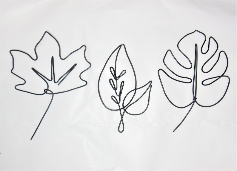 May include: Three wire sculptures of leaves. The leaves are made of black wire and are shaped like a maple leaf, a simple leaf, and a monstera leaf.