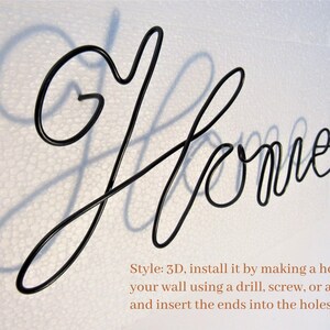 May include: Black metal wire sculpture of the word "Home" with a shadow cast on a white background. The sculpture is 3D and can be installed by making a hole in the wall and inserting the ends into the holes.