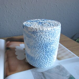 May include: A white ceramic jar with a blue and white marbled design. The jar has a textured surface and a lid.