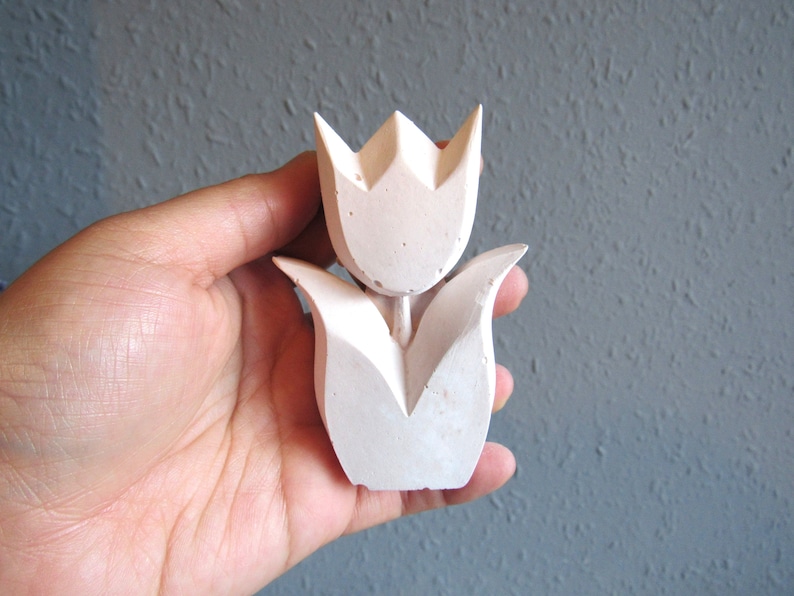 K&ouml;nnte beinhalten: Eine wei&szlig;e Tulpen-Skulptur aus Beton mit einem einfachen, geometrischen Design. Die Skulptur ist etwa 10 cm hoch und eignet sich perfekt, um Ihrem Zuhause einen Hauch von modernem Landhausstil zu verleihen.