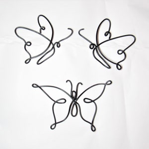 May include: Three black wire butterflies, each with a unique design, are displayed on a white background.