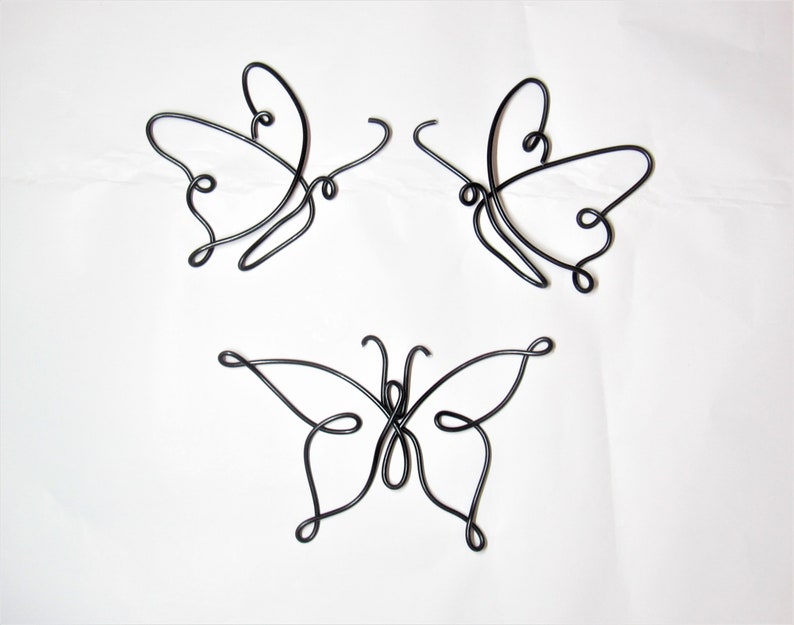 May include: Three black wire butterflies, each with a unique design, are displayed on a white background.