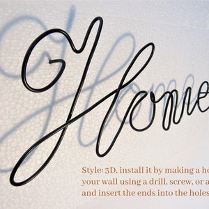 May include: Black metal wire sculpture of the word "Home" with a shadow cast on a white background. The sculpture is 3D and can be installed by making a hole in the wall and inserting the ends into the holes.