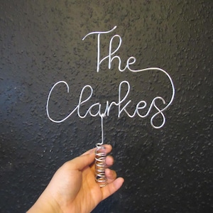 May include: A silver wire sculpture of the words "The Clarkes" with a spring attached to the bottom.