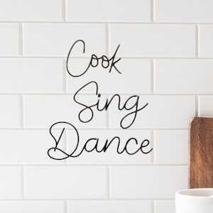 May include: White tile wall with black cursive writing that says "Cook Sing Dance".