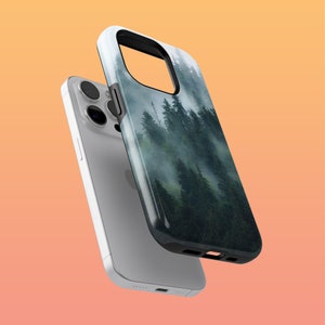Könnte beinhalten: Smartphone-Hülle mit einer nebligen Waldszene mit hohen grünen Bäumen. Die Hülle hat einen schwarzen Rand und eine glänzende Oberfläche. Das Telefon ist silber.