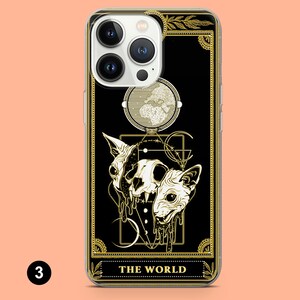 May include: A black phone case with a gold design featuring a tarot card with the number 3 and the words "THE WORLD". The card depicts a skull with two cat heads, a crescent moon, and a circle with stars.